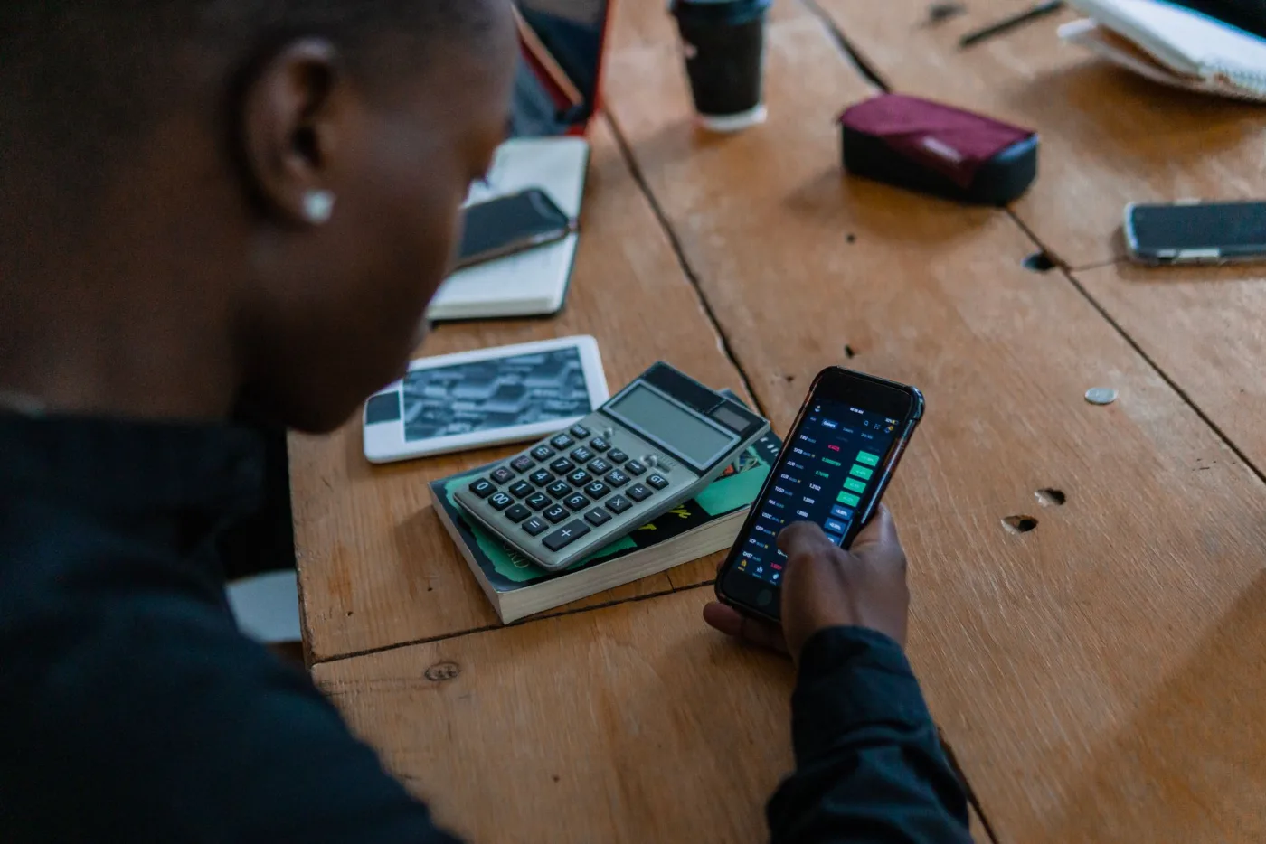 Ein Trader prüft Kurse am Handy neben einem Taschenrechner
